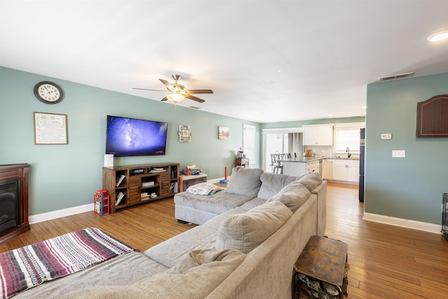 living area with ceiling fan, visible vents, baseboards, and hardwood / wood-style flooring