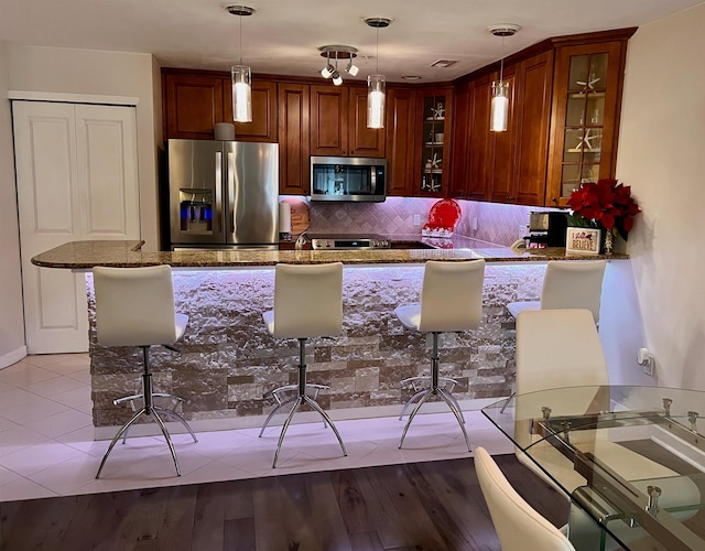 kitchen featuring stone counters, stainless steel appliances, hanging light fixtures, backsplash, and glass insert cabinets