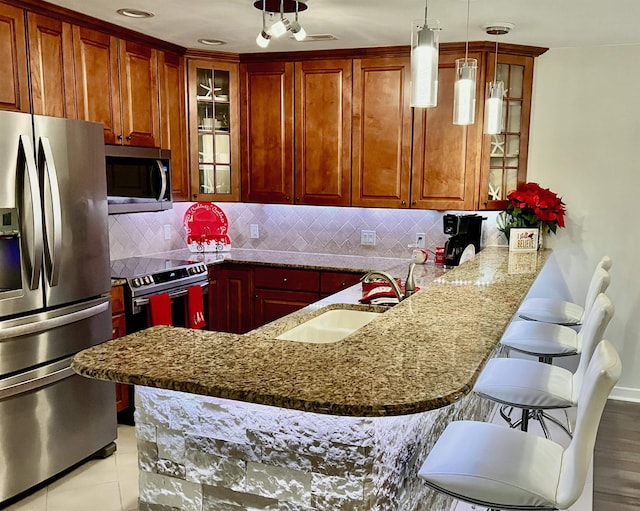 kitchen featuring a peninsula, a sink, appliances with stainless steel finishes, a kitchen bar, and glass insert cabinets