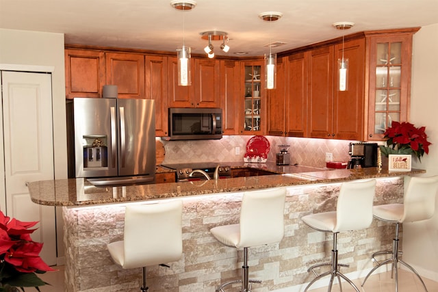 kitchen featuring decorative light fixtures, a breakfast bar area, stainless steel appliances, glass insert cabinets, and a peninsula