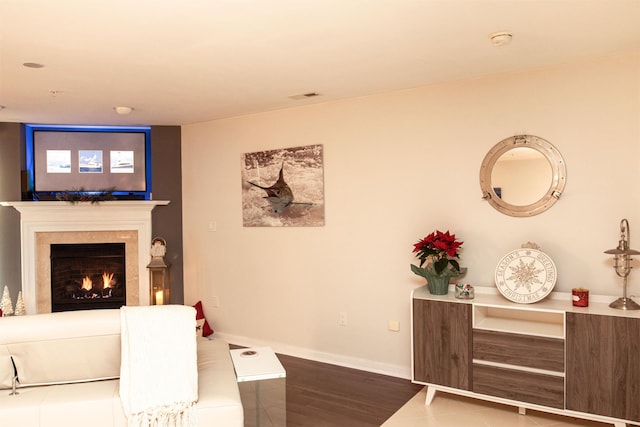 living area featuring a warm lit fireplace, wood finished floors, visible vents, and baseboards