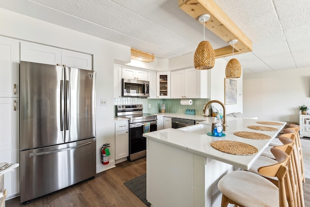 kitchen featuring stainless steel appliances, a peninsula, a sink, a textured ceiling, and a kitchen breakfast bar