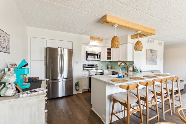 kitchen with appliances with stainless steel finishes, a sink, a peninsula, glass insert cabinets, and dark wood finished floors
