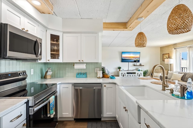 kitchen with appliances with stainless steel finishes, a sink, white cabinets, light stone countertops, and open floor plan