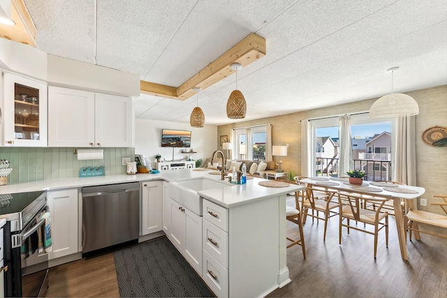 kitchen with appliances with stainless steel finishes, a sink, a peninsula, dark wood-style flooring, and a textured ceiling