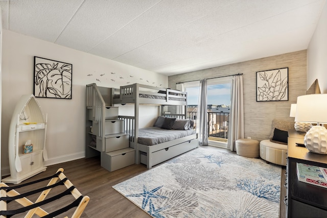 bedroom with access to outside, wood finished floors, baseboards, and a textured ceiling