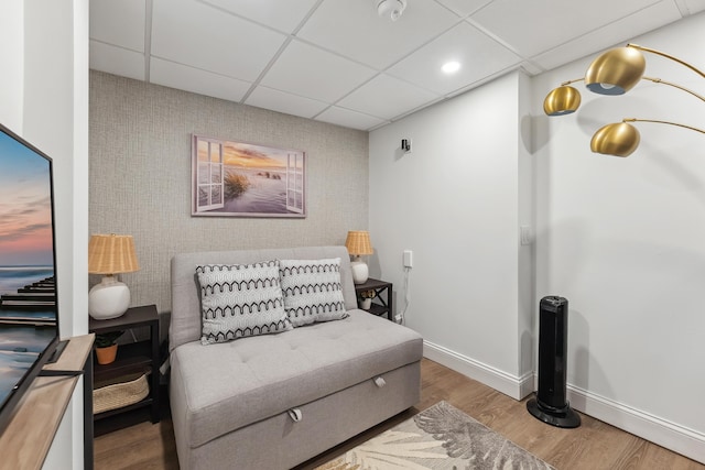 living area with a paneled ceiling, wood finished floors, an accent wall, and baseboards