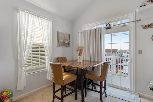 dining area featuring a healthy amount of sunlight, lofted ceiling, and light carpet