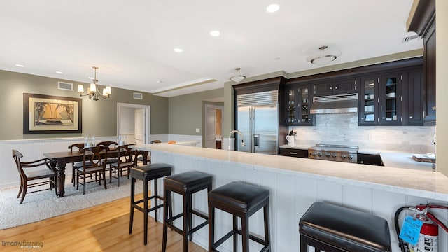 kitchen with under cabinet range hood, a wainscoted wall, visible vents, a kitchen breakfast bar, and stainless steel built in refrigerator