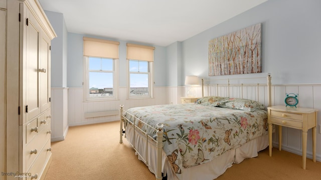 bedroom featuring a wainscoted wall and light carpet