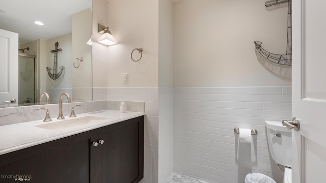 bathroom with toilet, a wainscoted wall, vanity, a shower stall, and tile walls