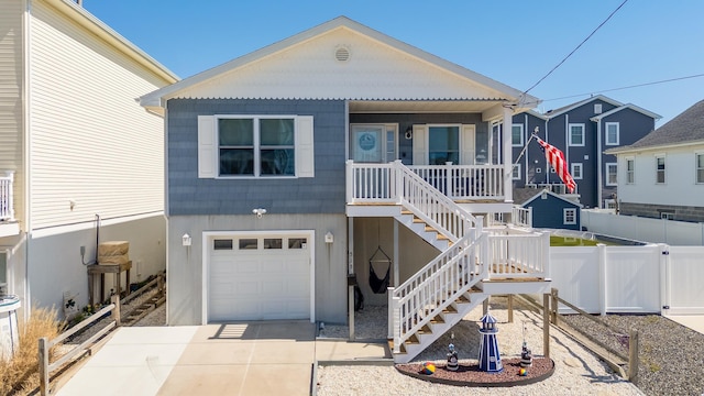 raised beach house with covered porch, stairway, fence, an attached garage, and driveway
