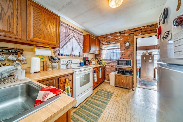 kitchen featuring brick wall, white electric range, refrigerator, and sink