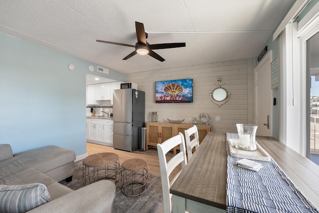 living room featuring sink, ceiling fan, a textured ceiling, light wood-type flooring, and wood walls