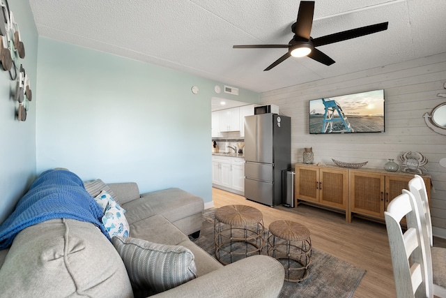 living room featuring sink, light hardwood / wood-style flooring, ceiling fan, wooden walls, and a textured ceiling