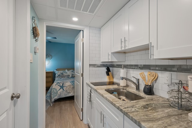 kitchen featuring white cabinetry, sink, backsplash, light hardwood / wood-style floors, and light stone countertops