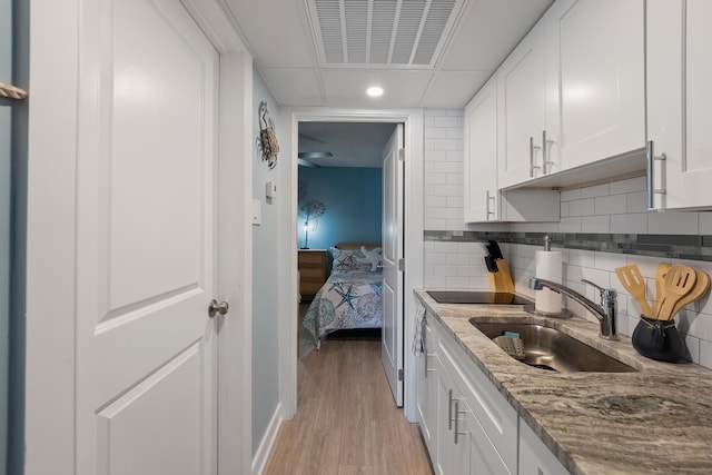 kitchen featuring sink, white cabinetry, light stone countertops, light hardwood / wood-style floors, and backsplash