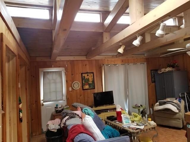 living area featuring wood ceiling, wooden walls, and beam ceiling