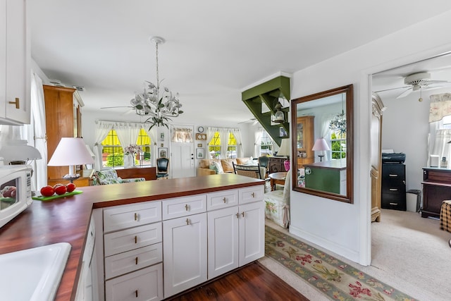 kitchen with ceiling fan with notable chandelier, a peninsula, open floor plan, white cabinetry, and white microwave
