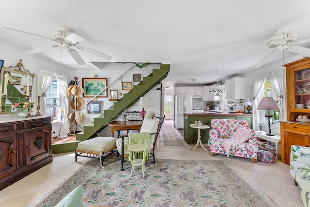 living room featuring a ceiling fan, stairs, and light colored carpet