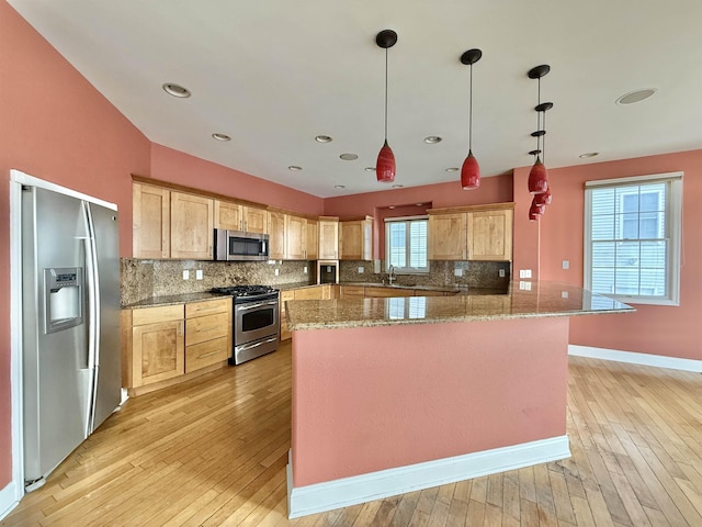 kitchen with light wood-type flooring, stainless steel appliances, pendant lighting, light brown cabinets, and a kitchen island