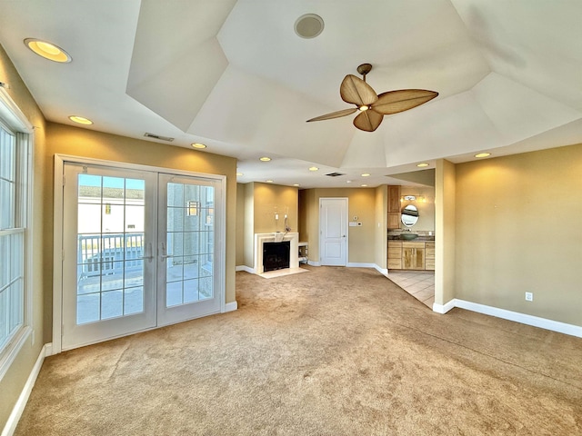 unfurnished living room featuring french doors, a tray ceiling, ceiling fan, and light colored carpet