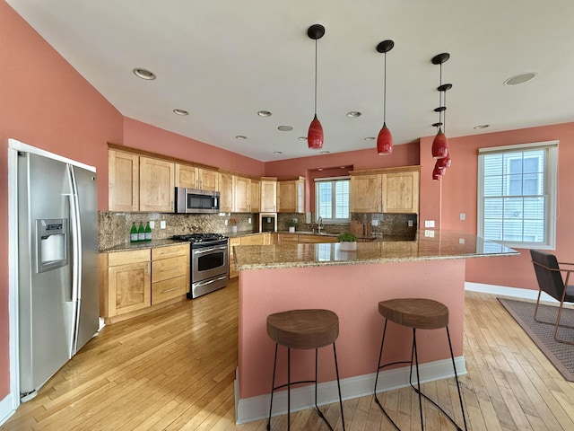 kitchen featuring pendant lighting, light brown cabinets, light stone counters, and appliances with stainless steel finishes