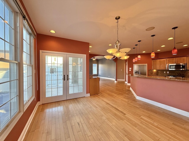 kitchen with an inviting chandelier, backsplash, decorative light fixtures, appliances with stainless steel finishes, and light wood-type flooring