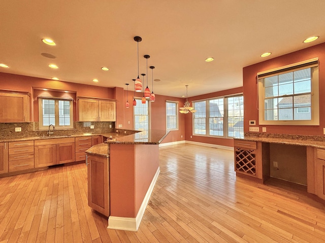 kitchen with decorative backsplash, light wood-type flooring, sink, decorative light fixtures, and dark stone countertops