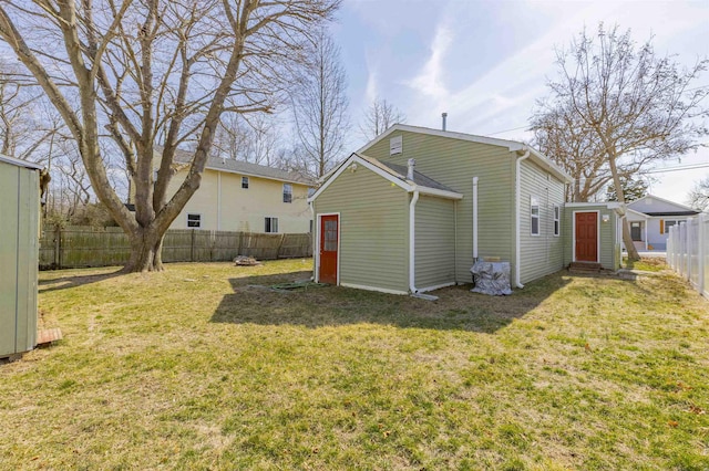 rear view of property featuring entry steps, fence, and a lawn