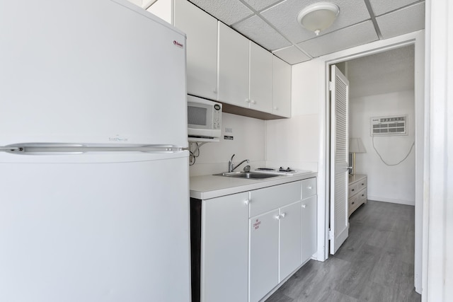 kitchen with sink, white cabinetry, a wall mounted AC, light hardwood / wood-style flooring, and white appliances