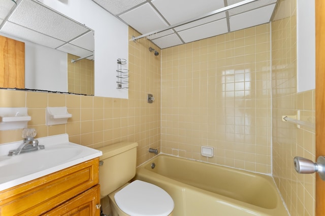 full bathroom with tile walls, tiled shower / bath combo, vanity, toilet, and a drop ceiling