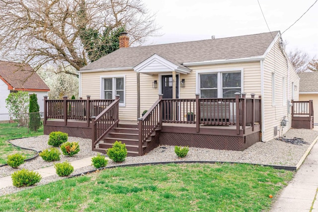 view of front of property with a chimney, a front lawn, a wooden deck, and roof with shingles