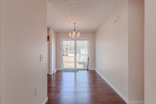 unfurnished dining area featuring dark wood finished floors, a notable chandelier, a textured ceiling, and baseboards