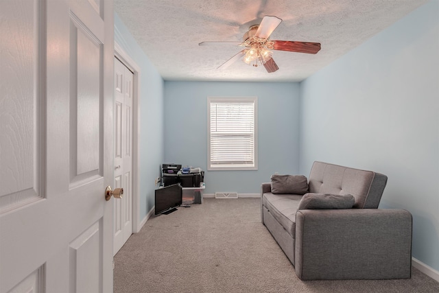 sitting room with a textured ceiling, carpet flooring, visible vents, and ceiling fan