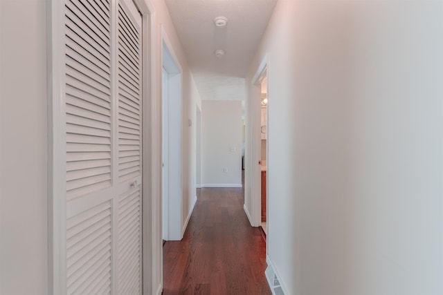 hall with visible vents, baseboards, and dark wood-style flooring