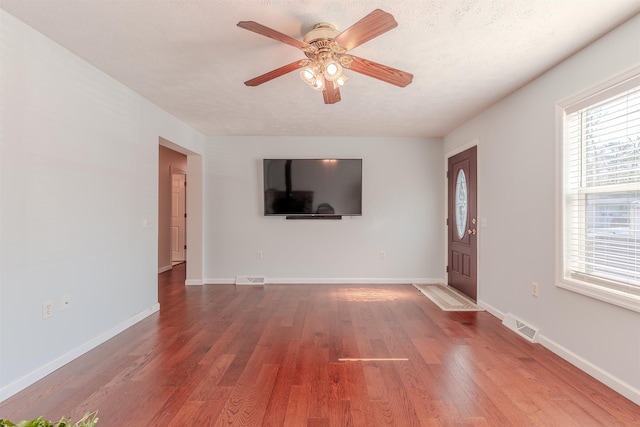 unfurnished living room featuring a textured ceiling, a ceiling fan, baseboards, and wood finished floors