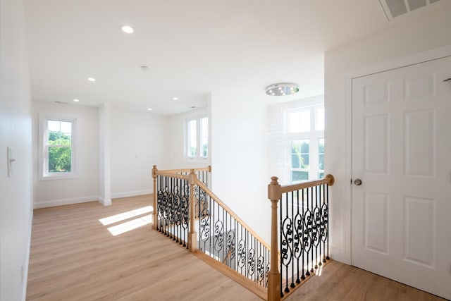 hall with visible vents, light wood finished floors, an upstairs landing, and a healthy amount of sunlight