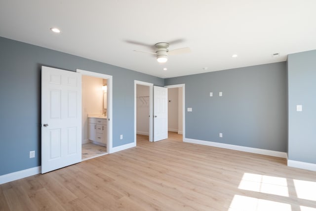 unfurnished bedroom featuring baseboards, light wood-style flooring, a walk in closet, a closet, and recessed lighting