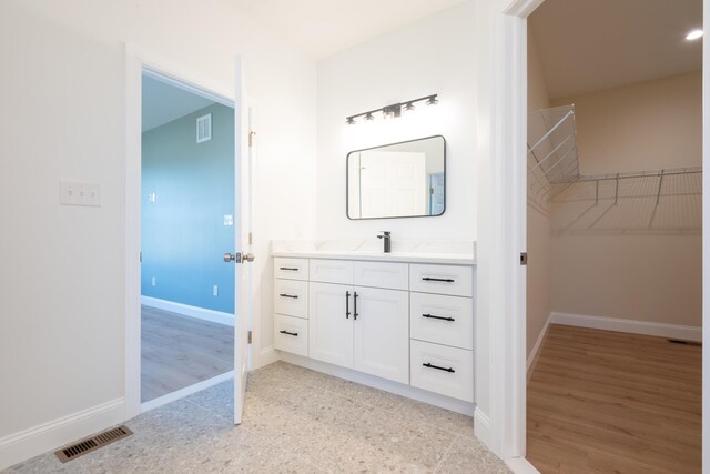 bathroom with baseboards, visible vents, a walk in closet, and vanity