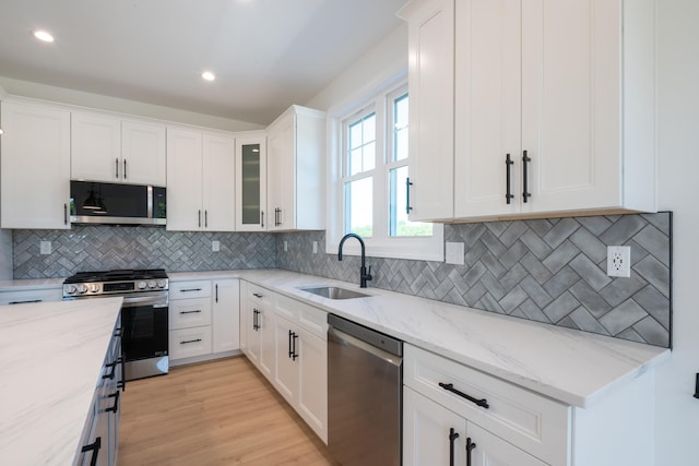 kitchen with stainless steel appliances, white cabinetry, a sink, and light stone counters