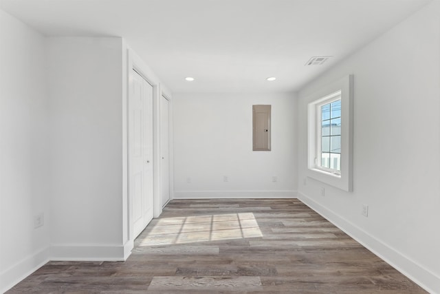 empty room with visible vents, wood finished floors, electric panel, and baseboards