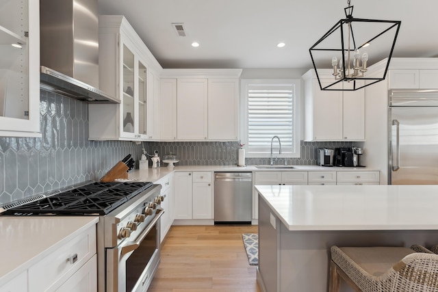 kitchen featuring pendant lighting, a breakfast bar, high end appliances, wall chimney range hood, and white cabinetry