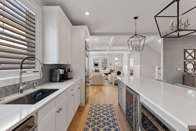 kitchen with pendant lighting, sink, beamed ceiling, white cabinetry, and beverage cooler