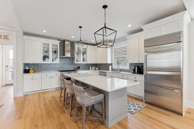 kitchen featuring wall chimney range hood, a kitchen island, a kitchen bar, white cabinets, and appliances with stainless steel finishes