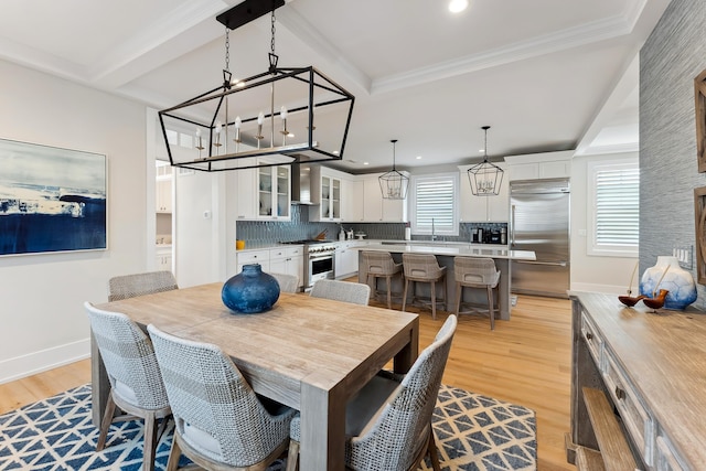 dining space with beam ceiling, sink, light hardwood / wood-style floors, and ornamental molding