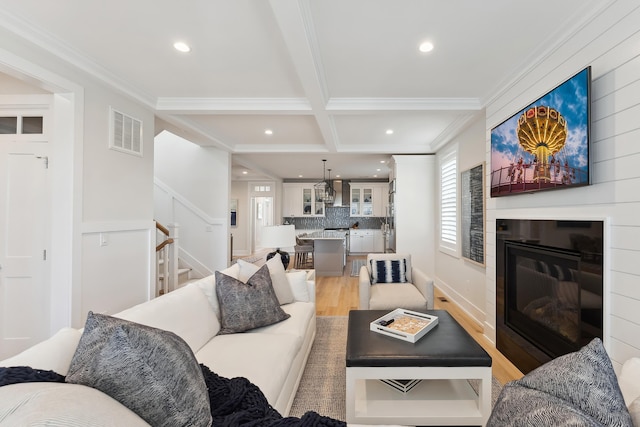 living room with a large fireplace, coffered ceiling, beamed ceiling, light wood-type flooring, and ornamental molding