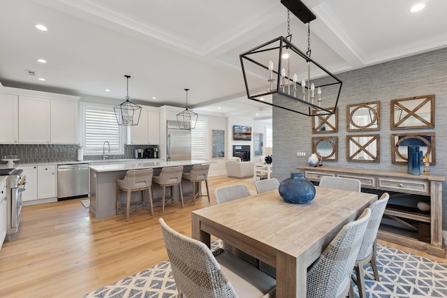 dining room with beamed ceiling, light wood-type flooring, ornamental molding, and sink