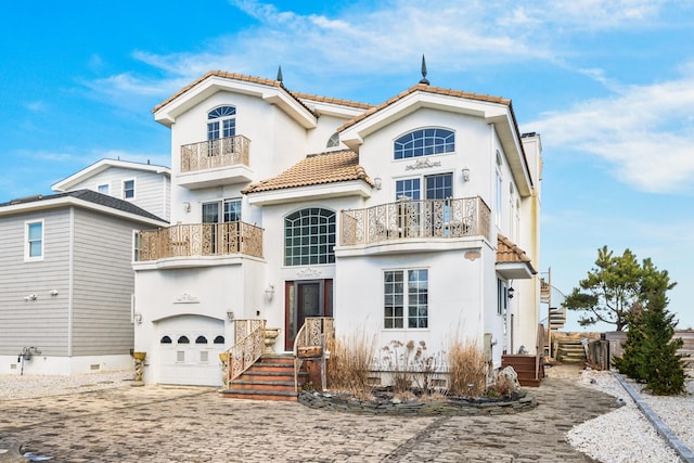 view of front of property with stucco siding, a tile roof, decorative driveway, an attached garage, and a balcony