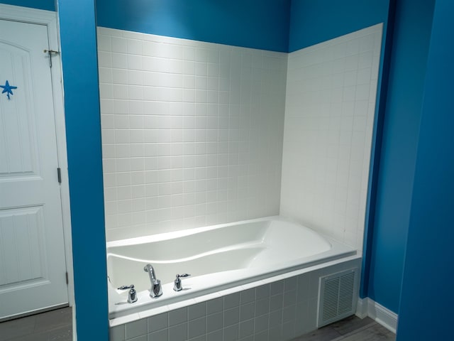 full bath featuring baseboards, wood finished floors, visible vents, and tiled tub